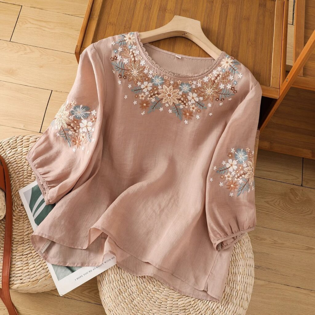 Beige blouse with floral embroidery on hanger.