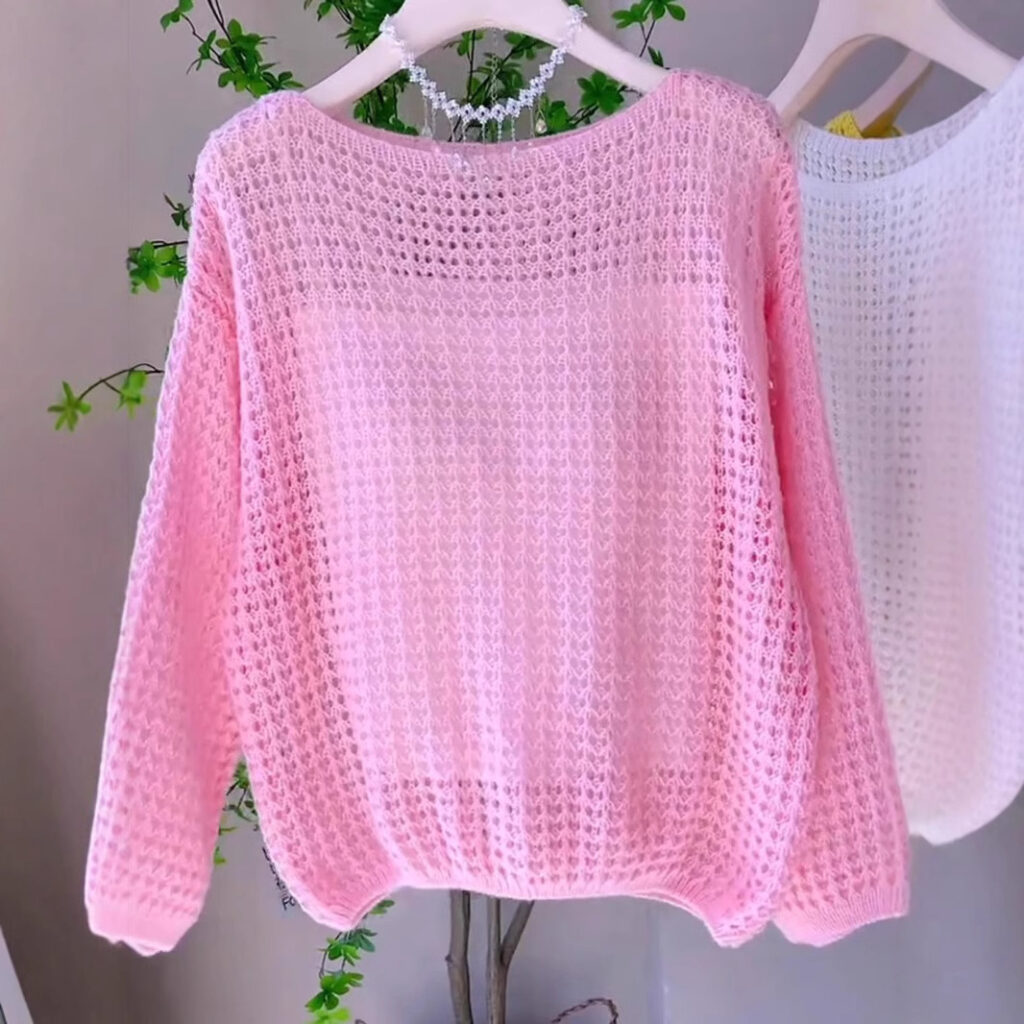Pink crochet sweater on hanger.