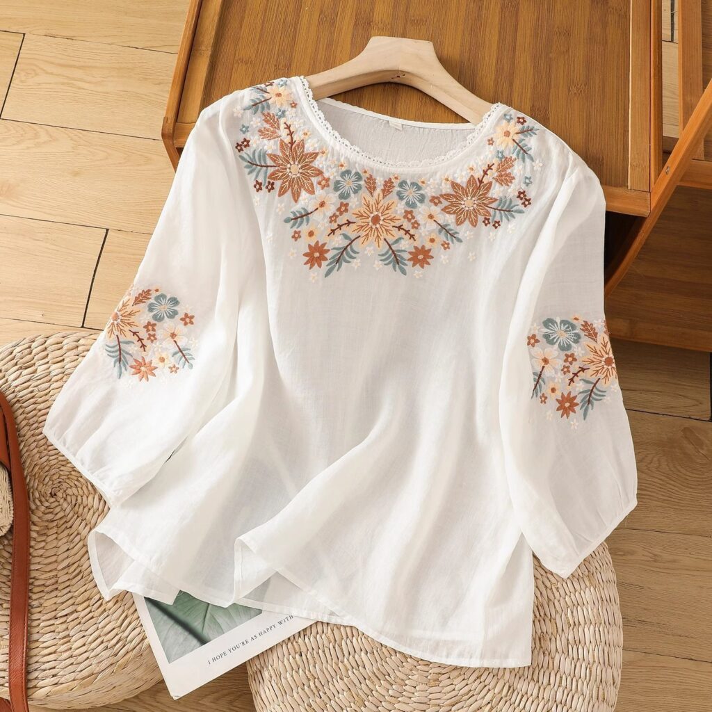 White blouse with floral embroidery on hanger.