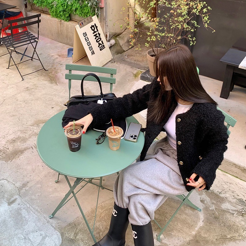 Woman sitting at a green table with iced coffee drinks outdoors.