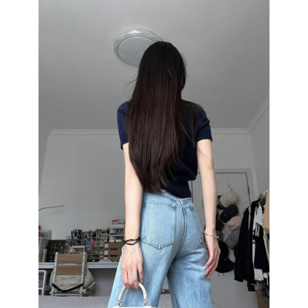 Woman standing in room, long hair, jeans.