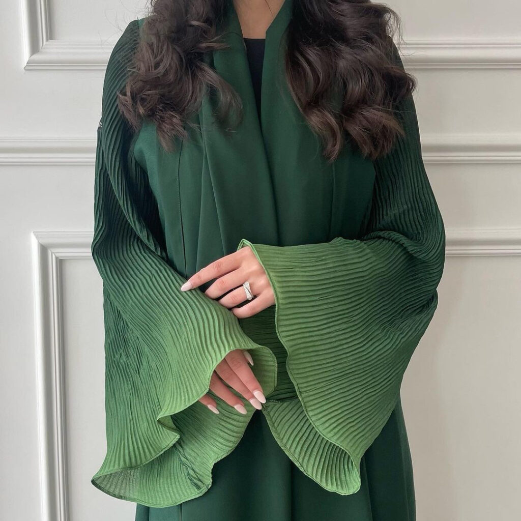 Woman in green pleated dress, crossed arms.