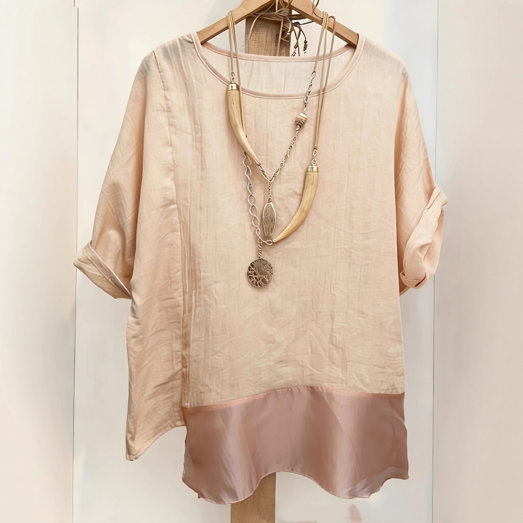 Beige blouse with necklace on hanger.