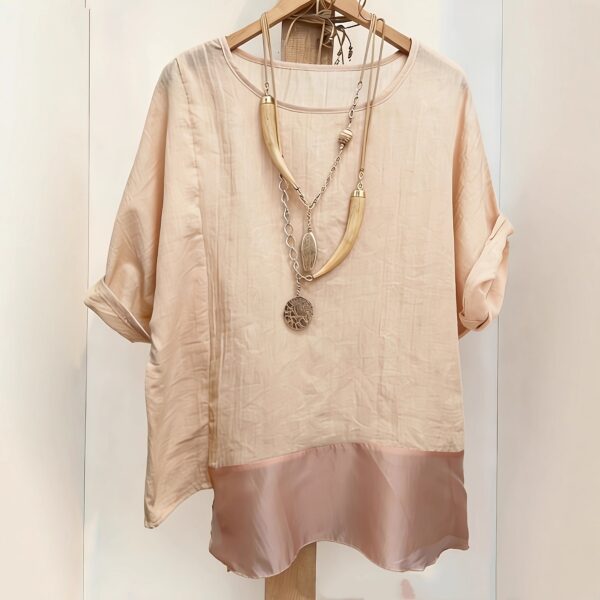 Beige blouse with necklace on hanger.