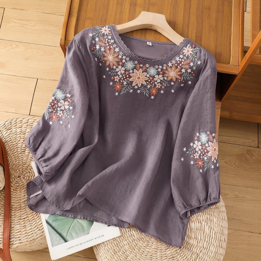 Purple blouse with floral embroidery on hanger.