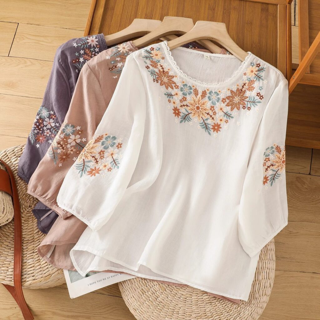 Embroidered floral blouses on wooden hangers.
