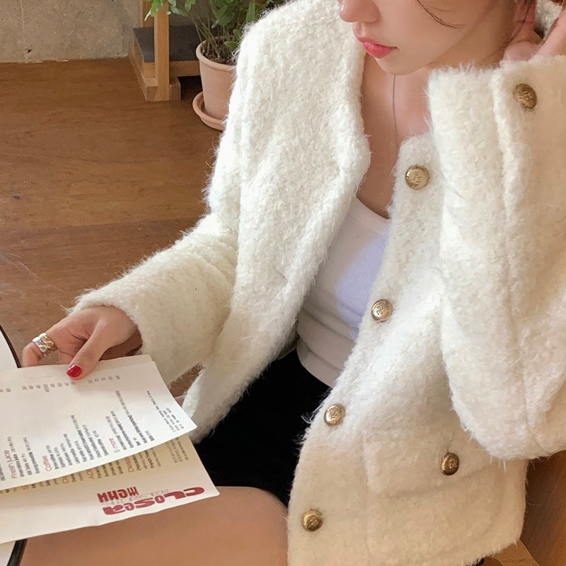 Person in a white textured coat reading a menu or booklet indoors.